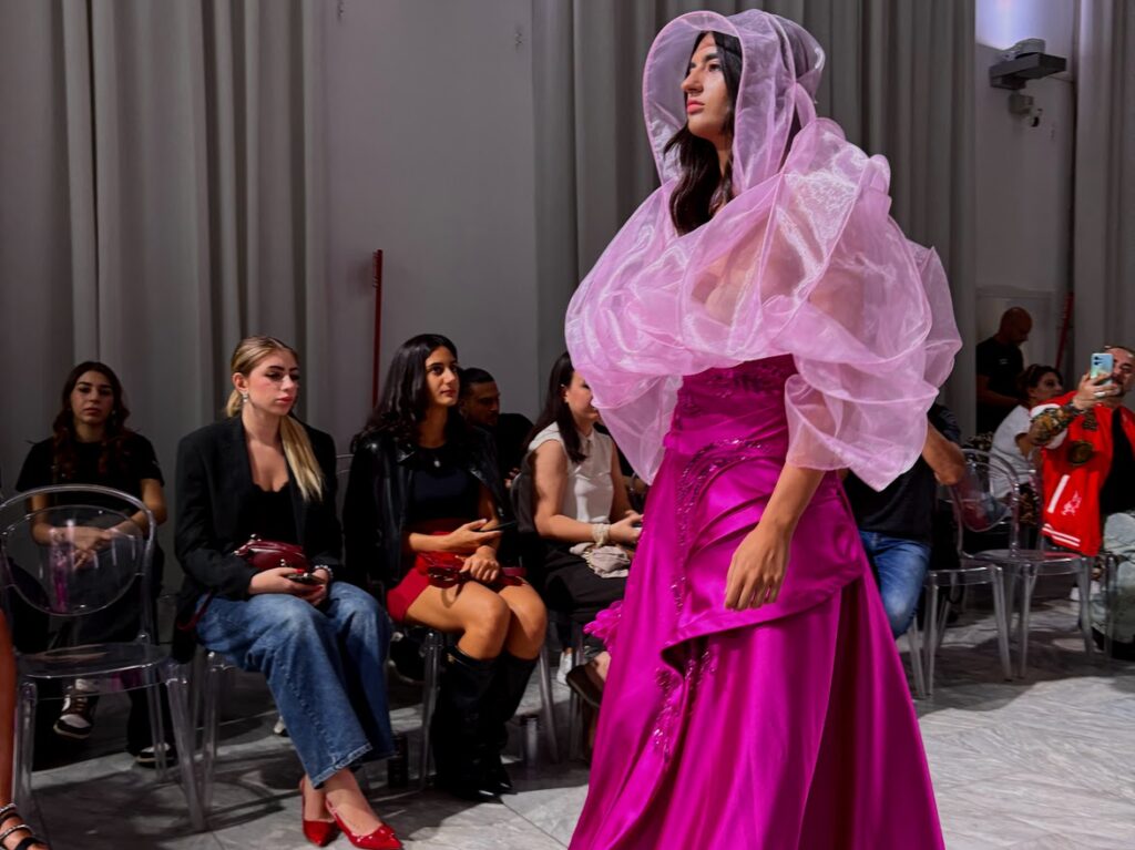 modella con un abito fucsia e una cappa con cappuccio rosa trasparente